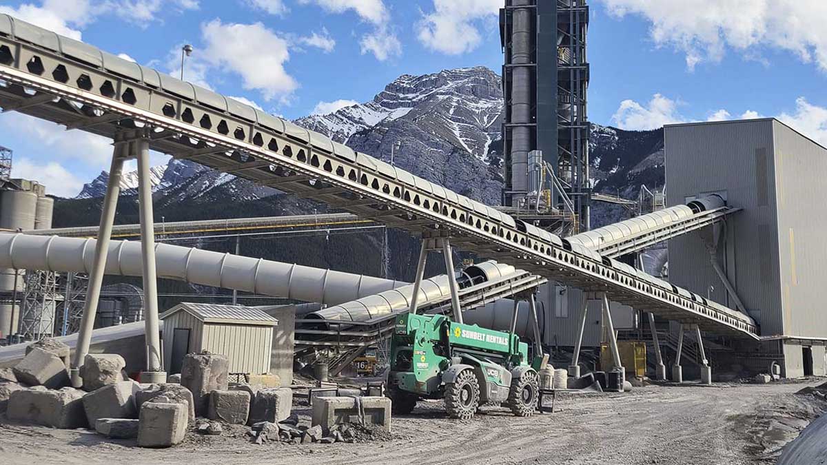 A conveyor belt and green truck move aggregate supplies at a plant in the mountains