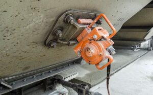 An orange railcar vibrator being used to unload a railcar