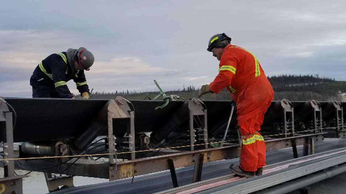 Two workers servicing a conveyer belt trough idler outside